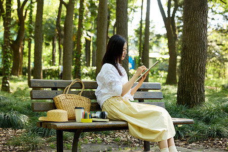 写生背景坐在森林长椅上画画的女孩背景