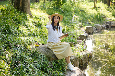 草帽女坐在小溪边石头上画画的美女背景