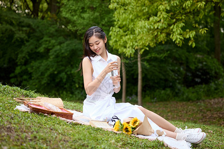 治愈春日在野餐垫上喝水休息的美女形象背景