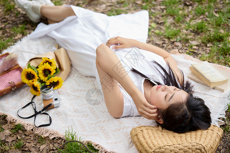 户外躺在野餐垫上听歌休息的美女背景图片