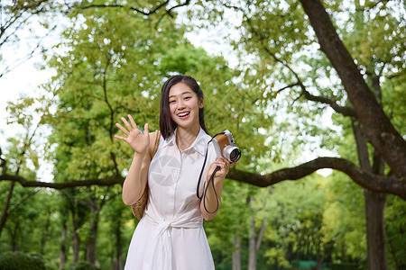 绿色相机公园里拿着相机挥手的美女背景