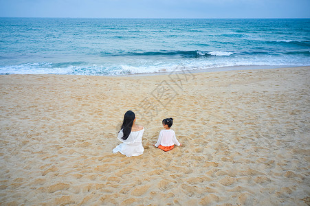 假期夏季坐在沙滩上的海边母女背影背景