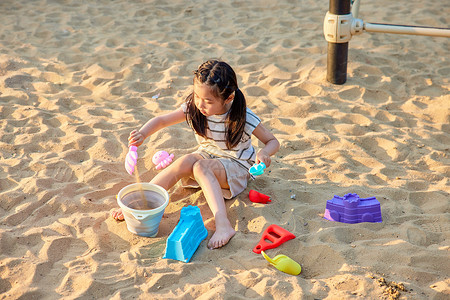 小女孩扎着双马尾在沙滩上玩沙子图片