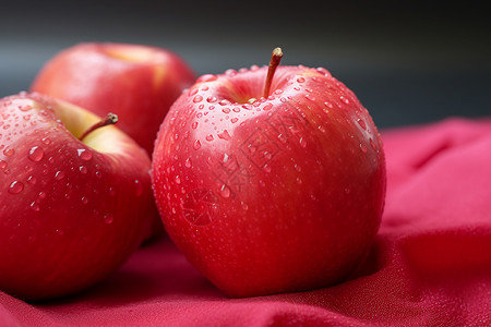 两颗红苹果红布黑底滴落水珠的诱人水果图片